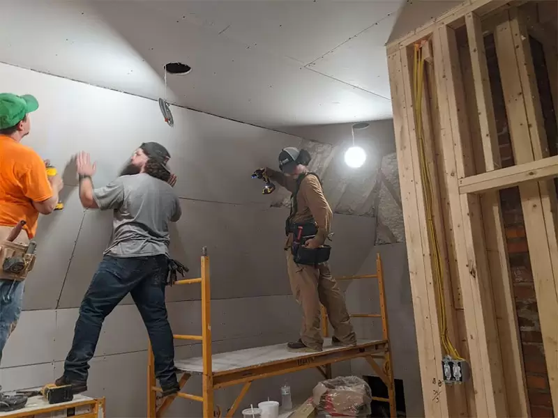 Our crew hanging drywall sheets on scaffolding during a room build out