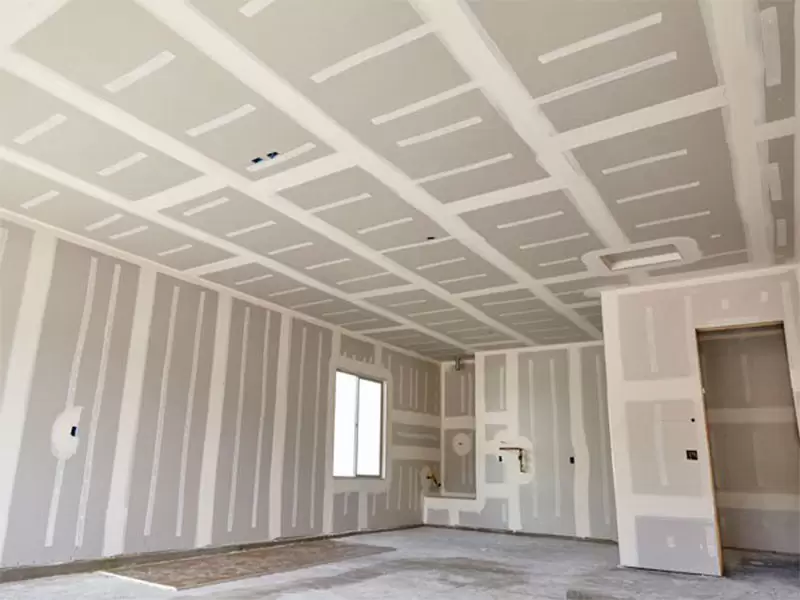 Sanding a freshly mudded ceiling seam by a sunlit window
